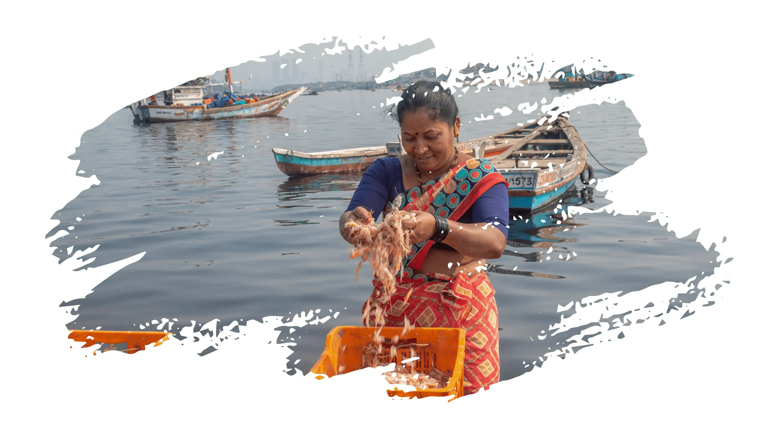 Koli fisherwoman cleaning fresh prawns at Worli Koliwada with traditional fishing boats in the background.